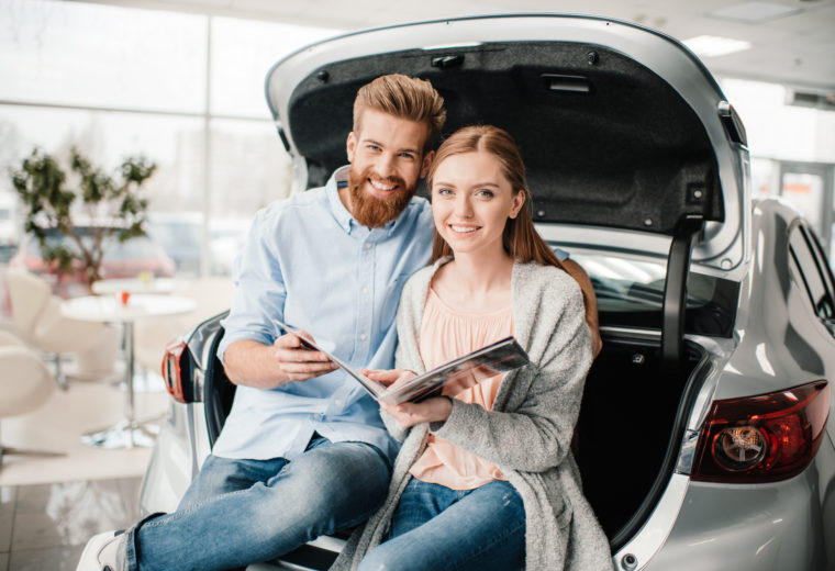 couple in the trunk of a new car with auto insurance. 